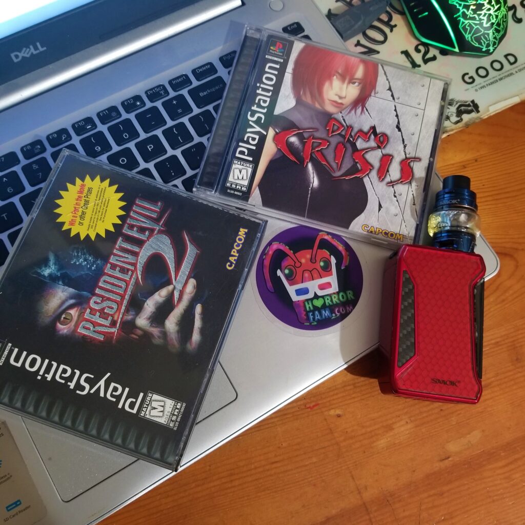 Resident Evil 2, Dino Crisis, a laptop, a HorrorFam.com sticker, and a vape mod