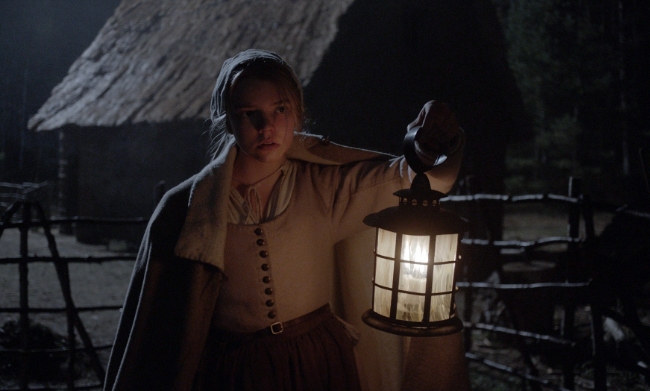 Screenshot from The Witch / The VVitch of a puritan girl holding up a lantern in the dark
