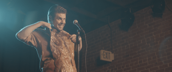 Charlie in Cannibal Comedian holding up a slice of human skin on stage